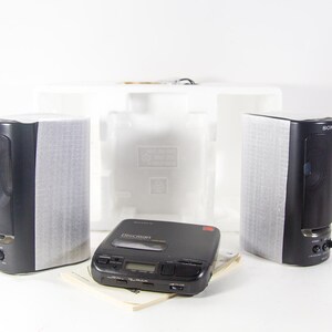 May include: A black Sony Discman CD player with a red display and buttons. The player is surrounded by white polystyrene packaging and two black speakers.