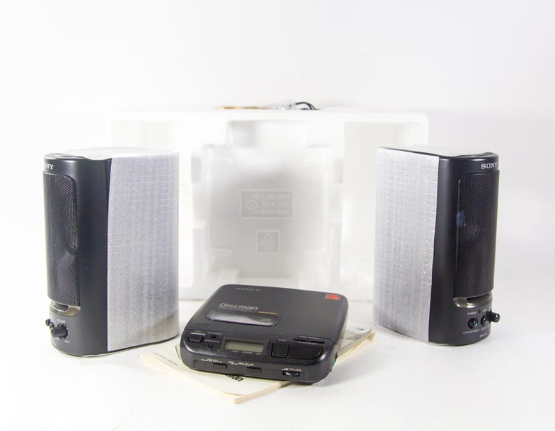 May include: A black Sony Discman CD player with a red display and buttons. The player is surrounded by white polystyrene packaging and two black speakers.