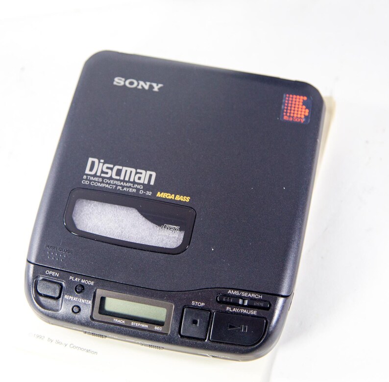 May include: A black Sony Discman CD player with the text "Discman 8 Times Oversampling CD Compact Player D-32 MEGA BASS" on the front. The player has a silver display screen and buttons for open, play mode, repeat/enter, stop, AMS/search, and play/pause.