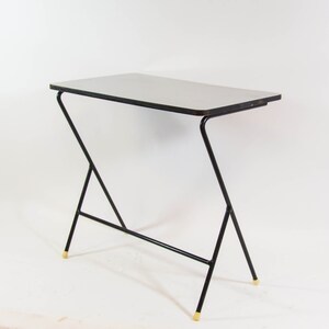 May include: A black metal table with a white top and gold accents. The table has a unique, angled design.