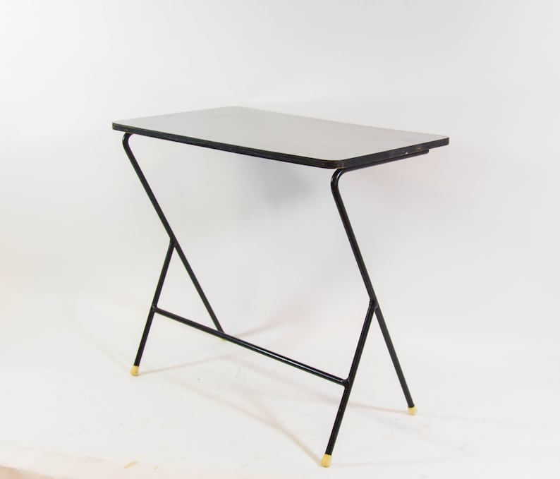 May include: A black metal table with a white top and gold accents. The table has a unique, angled design.