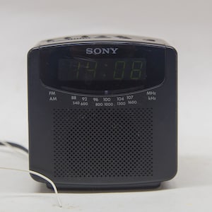 Könnte beinhalten: Ein schwarzes Sony-Radiowecker mit einem digitalen Display, das die Zeit 08:08 anzeigt. Das Radio hat ein Lautsprechergitter und ein Zifferblatt mit Frequenzmarkierungen für FM- und AM-Radiobänder.
