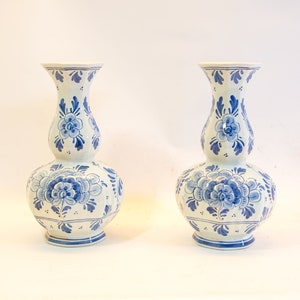Op de afbeelding: Twee witte keramische vazen met blauwe bloempatronen. De vazen hebben een bolvormige basis, een smaller middengedeelte en een uitlopende bovenkant. Het blauwe bloemendesign omvat gedetailleerde bloem- en bladmotieven, met accenten van kleine stippen.