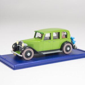May include: A green toy car model with black accents and white wheels. The car is on a blue display base.