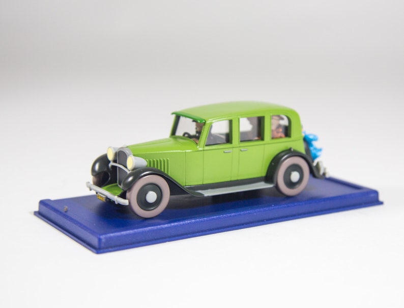 May include: A green toy car model with black accents and white wheels. The car is on a blue display base.