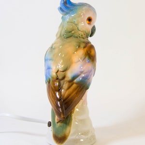 May include: A ceramic parrot lamp with a blue, green, and brown color scheme. The parrot is perched on a branch and has a white base.