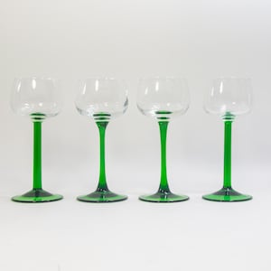 May include: Four clear glass wine glasses with green stems and bases. The glasses are arranged in a row on a white background.