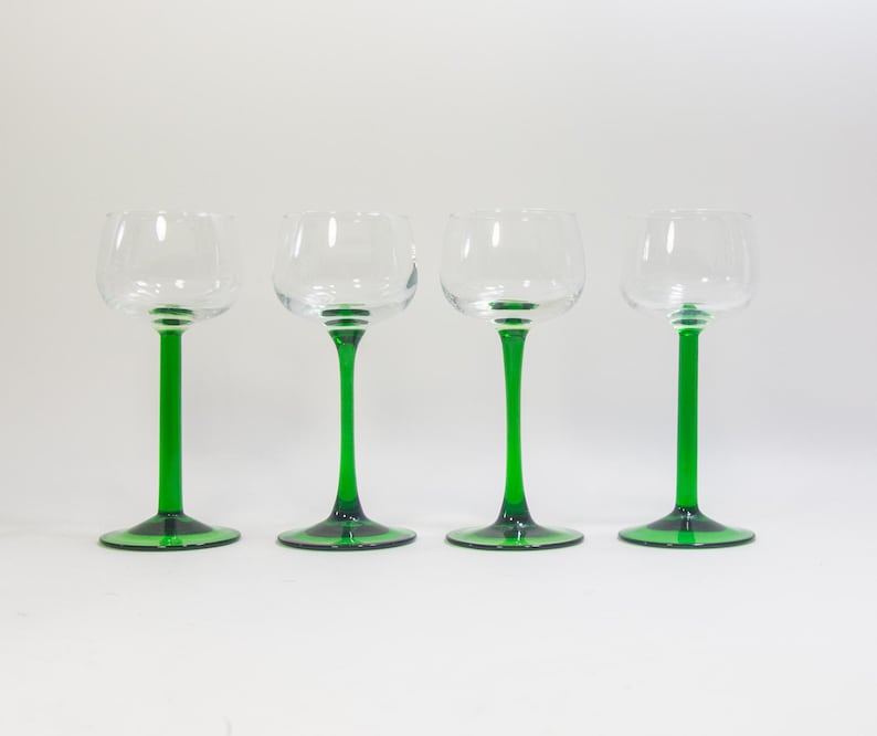 May include: Four clear glass wine glasses with green stems and bases. The glasses are arranged in a row on a white background.