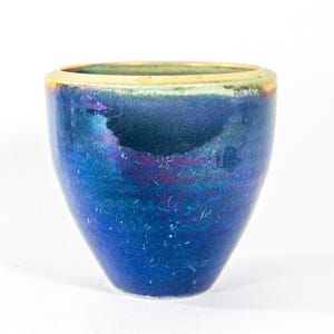 Könnte beinhalten: Eine blaue Keramikvase mit goldfarbenem Rand. Die Vase hat eine leicht irisierende Oberfläche und eine abgerundete Form.