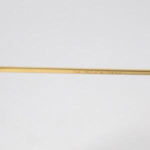 May include: Close-up of the gold-tone metal arm of a pair of glasses. The arm is engraved with the text "1114 34-24-145 3N 59014".