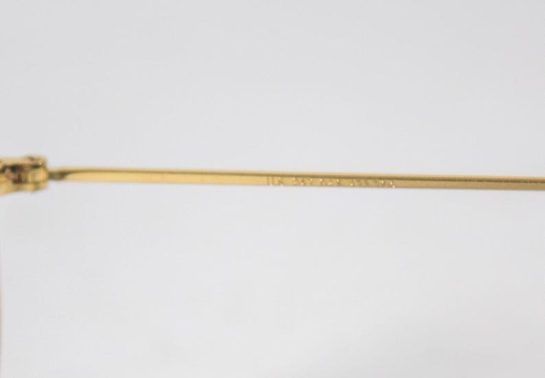 May include: Close-up of the gold-tone metal arm of a pair of glasses. The arm is engraved with the text "1114 34-24-145 3N 59014".