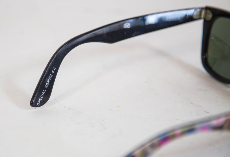 Puede incluir: Gafas de sol negras con acabado brillante en la patilla. El interior de la patilla tiene impreso el texto en blanco SPECIAL SERIES # 4. Un peque&ntilde;o logotipo circular es visible cerca de la bisagra. La montura incluye lentes de color verde oscuro.