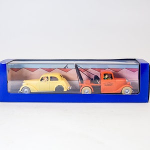 Puede incluir: Un coche amarillo siendo remolcado por una gr&uacute;a naranja. Ambos veh&iacute;culos est&aacute;n en una caja de pl&aacute;stico transparente con fondo azul. La gr&uacute;a tiene la palabra "LUXOR" impresa en el lateral.
