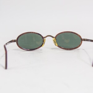 May include: Brown oval-shaped sunglasses with green lenses. The frame is made of a brown tortoiseshell material.