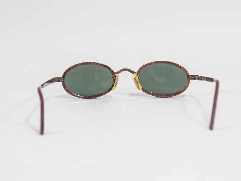May include: Brown oval-shaped sunglasses with green lenses. The frame is made of a brown tortoiseshell material.