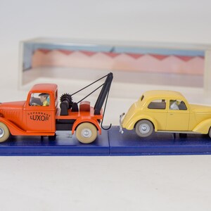Puede incluir: Un cami&oacute;n de remolque rojo con un coche amarillo que est&aacute; siendo remolcado. El cami&oacute;n de remolque tiene la palabra "LUXOR" en el lateral. Ambos veh&iacute;culos est&aacute;n sobre una base de exposici&oacute;n azul.