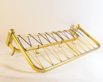 May include: A gold metal coat rack with a black and yellow string design. The rack has a curved shape and multiple hooks.