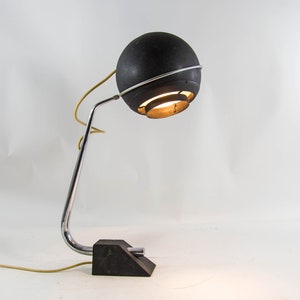 May include: A black and silver desk lamp with a spherical shade. The shade has a ring around it and a small light inside. The lamp has a curved arm and a black base.