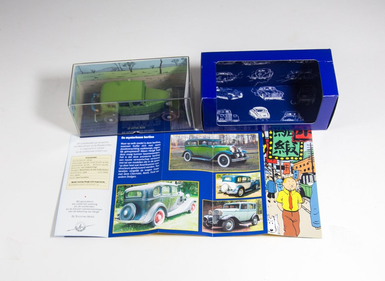 May include: A green and black model car in a clear plastic box with a blue and white box next to it. The blue box has a picture of a car on it. The boxes are on a white surface. The model car is a 1930s Dodge Brothers Coupe.