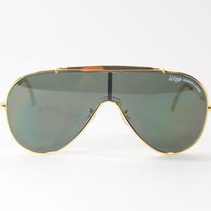 May include: Gold-framed aviator sunglasses with green lenses. The sunglasses have a 'Wings' logo on the right frame.
