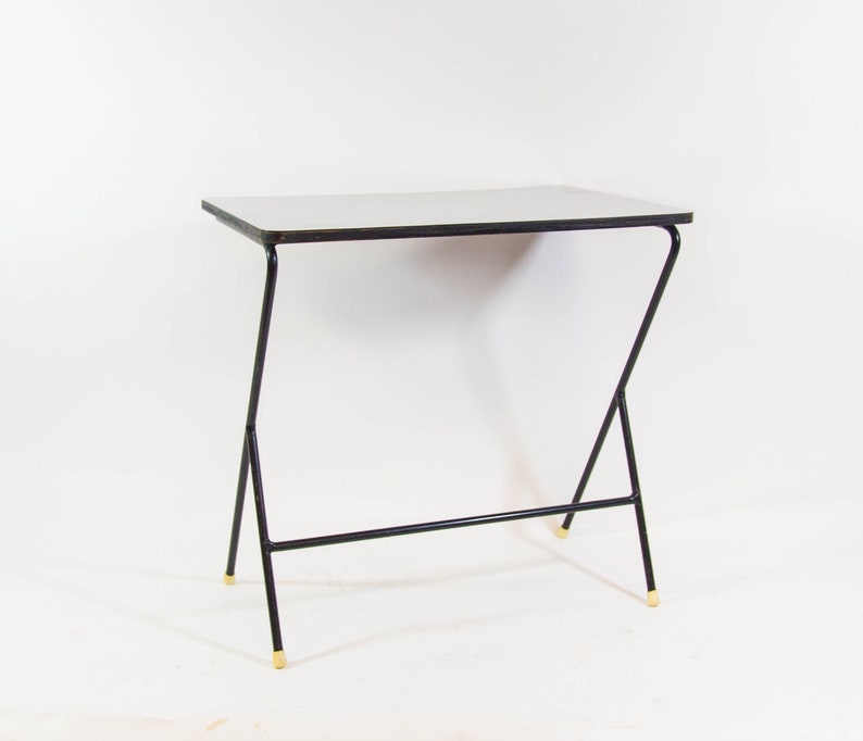 May include: A white table with a black metal frame and gold-coloured tips on the legs. The table has a simple, modern design.