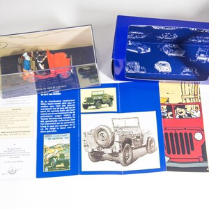 May include: A red toy jeep in a clear display case. The jeep has two figures inside. The case is on a blue and white background with text that reads 'The Universal Jeep' and 'All the Facts of the War'.