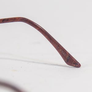May include: Close-up of the brown tortoiseshell temple tip of a pair of eyeglasses. The temple tip is inscribed with the text "77320 DAD & CO."