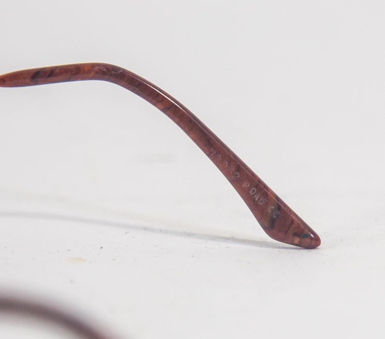 May include: Close-up of the brown tortoiseshell temple tip of a pair of eyeglasses. The temple tip is inscribed with the text "77320 DAD & CO."