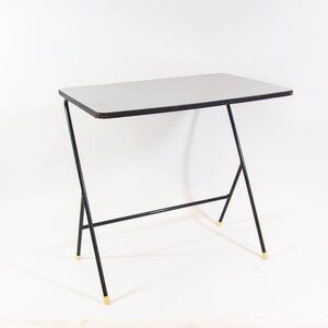 May include: A black metal table with a white laminate top. The table has a simple, modern design with a single shelf.