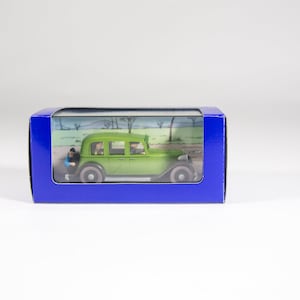 May include: A green toy car with a blue box. The car has a clear window and two figures inside. The box has a blue background and white text.