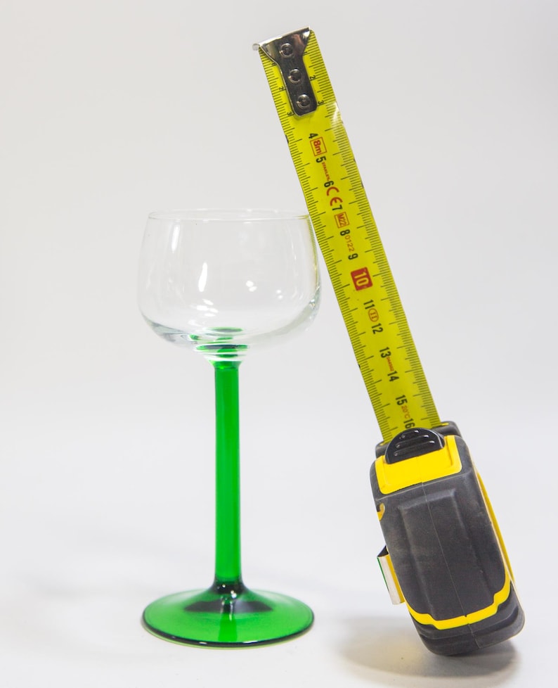 May include: A yellow tape measure with a black and yellow handle is next to a green stemmed wine glass. The tape measure is extended to 40 cm.
