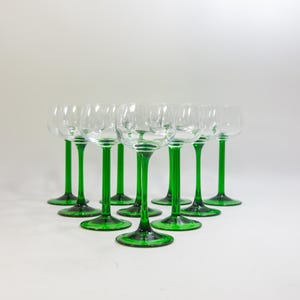 May include: Set of twelve clear glass stemmed drinking glasses with green stems. The glasses are arranged in a triangular pattern.