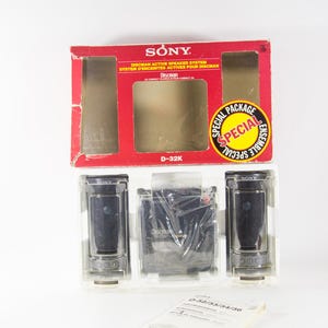 May include: A Sony Discman D-32K active speaker system in its original packaging. The box is red and white with the Sony logo and the words "Special Package" and "Ensemble Special". The system includes two black speakers and a black Discman player.