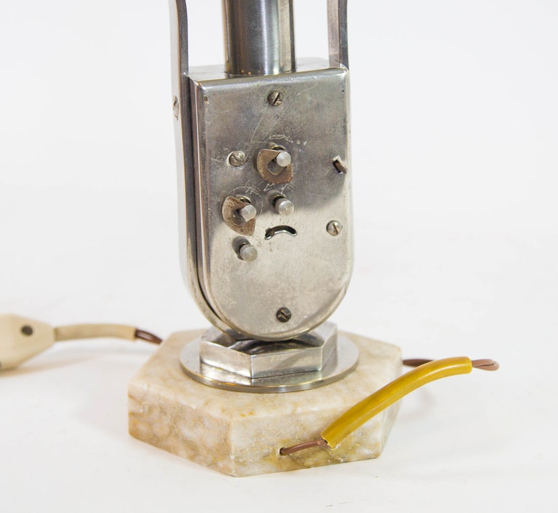 Peut inclure: Une lampe de table en argent et chrome avec une base en marbre et un cordon avec un fil jaune. La lampe a une base ronde en argent et une tige en chrome avec un abat-jour en argent.