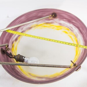 Pu&ograve; includere: Un lampadario vintage con un paralume circolare in vetro viola e giallo. L'apparecchio comprende una lampadina, bracci di supporto in metallo e un metro a nastro. Il diametro del paralume &egrave; di circa 38 cm.