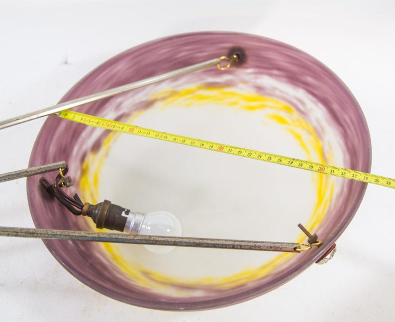 Pu&ograve; includere: Un lampadario vintage con un paralume circolare in vetro viola e giallo. L'apparecchio comprende una lampadina, bracci di supporto in metallo e un metro a nastro. Il diametro del paralume &egrave; di circa 38 cm.