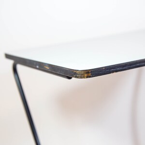 May include: Close-up of the edge of a white table top with a black metal frame. The table top has a slight chip in the white paint.