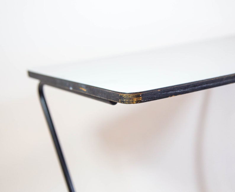 May include: Close-up of the edge of a white table top with a black metal frame. The table top has a slight chip in the white paint.