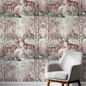 May include: A light grey armchair with wooden legs sits in front of wallpaper featuring a repeating pattern of deer, rabbits, and birch trees in shades of dusty pink, cream, and dark grey. The scene depicts a woodland forest with ferns.
