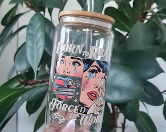 May include: A clear glass water bottle with a bamboo lid and a straw. The bottle has a comic book style graphic with a woman crying and the text "Born to Read, Forced to Work".