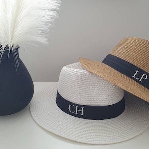 May include: Two straw hats with black ribbon bands. The white hat has the initials "CH" embroidered on the band. The brown hat has the initials "LP" embroidered on the band.