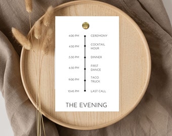 May include: A white card with a black vertical line and black dots marking the time. The card lists the schedule for an evening event, including a ceremony, cocktail hour, dinner, first dance, taco truck, and last call. The text "THE EVENING" is at the bottom of the card.