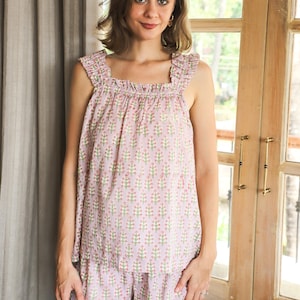 May include: A light purple sleeveless top and matching shorts set featuring a repeating floral pattern of small pink flowers with green stems. The top has a square neckline with ruffled shoulder straps, and the shorts feature a ruffled hemline.