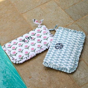 May include: Two rectangular decorative cushions with floral and patterned designs. One cushion features pink flowers on a white background with the initials "K/N" embroidered in green. The other has a blue pattern on a white background with a blue monogram.