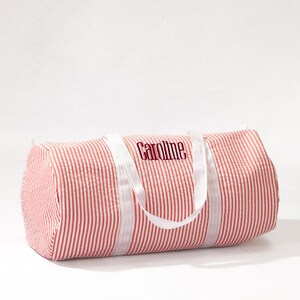 Puede incluir: Bolsa de deporte de lona a rayas rojas y blancas con asas blancas y el nombre "Caroline" bordado en rojo en la parte delantera.