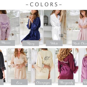 May include: A selection of satin robes in shades like light mauve, navy, white, and nude champagne. The robes have lace detailing on the sleeves and personalized text on the back, including "Mom of the Bride" and "Katie".