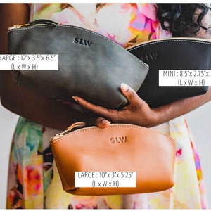 May include: Three leather cosmetic bags in different sizes. The largest bag is dark green, the medium bag is brown, and the smallest bag is black. The bags have a curved shape and a zipper closure. The bags are labeled with the text "SLW" and their dimensions in inches: X-LARGE: 12"x 3.5"x 6.5" (L x W x H), LARGE: 10"x 3"x 5.25" (L x W x H), MINI: 8.5"x 2.75"x 3.5" (L x W x H).