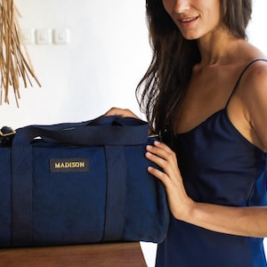 K&ouml;nnte beinhalten: Eine dunkelblaue Reisetasche mit einem goldenen Rei&szlig;verschluss und dem Schriftzug "MADISON" auf der Vorderseite.