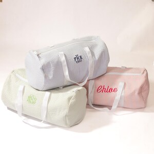 Puede incluir: Tres bolsas de lona rayadas con correas blancas. Las bolsas est&aacute;n personalizadas con los nombres "Chloe", "FRB" y un monograma.