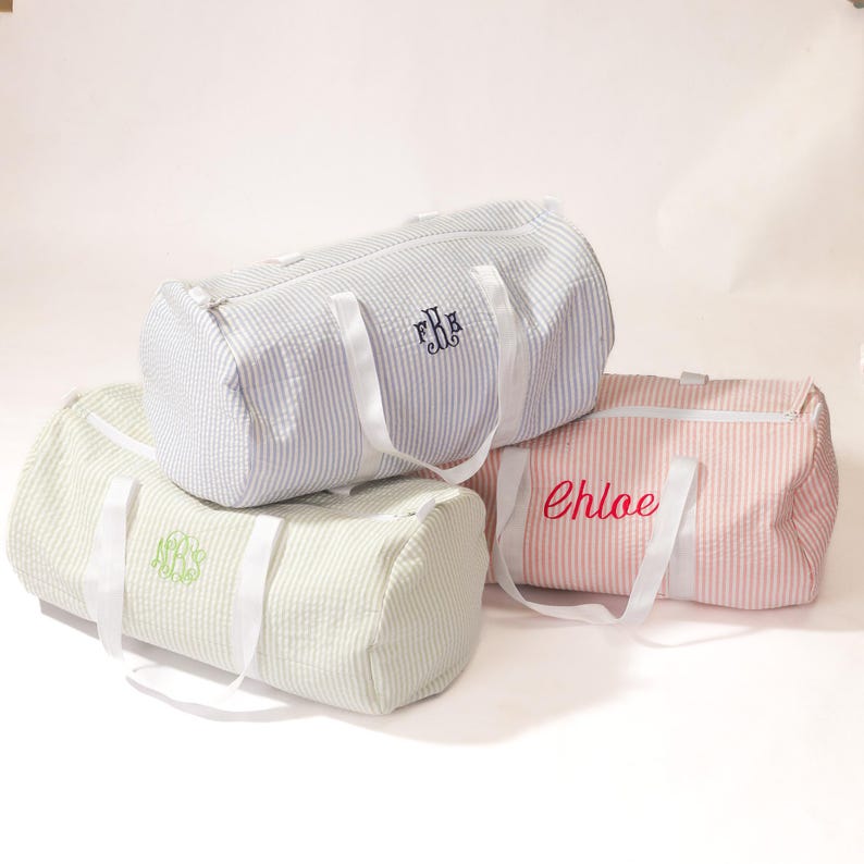 Puede incluir: Tres bolsas de lona rayadas con correas blancas. Las bolsas est&aacute;n personalizadas con los nombres "Chloe", "FRB" y un monograma.